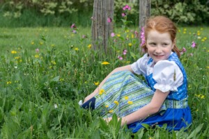 Ein junges Mädchen im Dirndl sitzt auf der Wiese