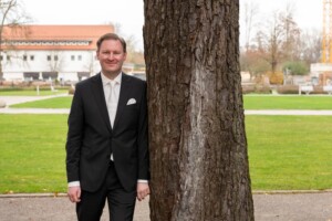 Glücklich lehnt der Bräutigam am Baum am Kloster Fürstenfeld